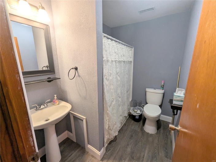Bathroom with wood finished floors, baseboards, toilet, a shower with shower curtain, and visible vents