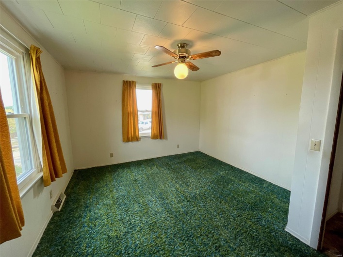 Empty room with ceiling fan, a wealth of natural light, dark colored carpet, and visible vents