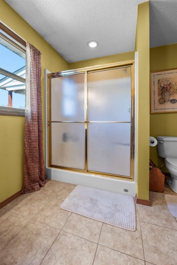 Bathroom with tile patterned floors, toilet, a textured ceiling, and a stall shower