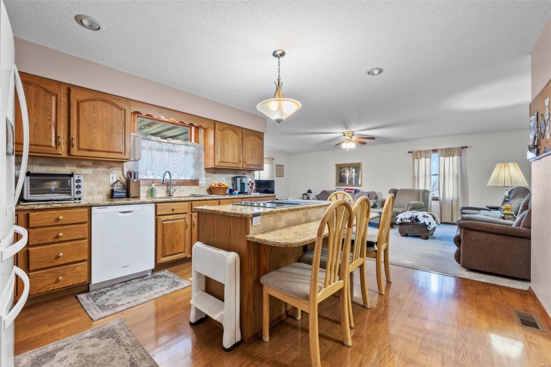Kitchen with light wood-type flooring, visible vents, a breakfast bar, white dishwasher, and open floor plan