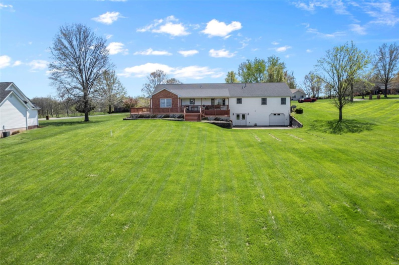 Rear view of house with a wooden deck, a garage, driveway, and a lawn