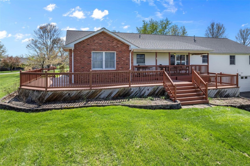 Rear view of house with brick siding, a deck, and a lawn