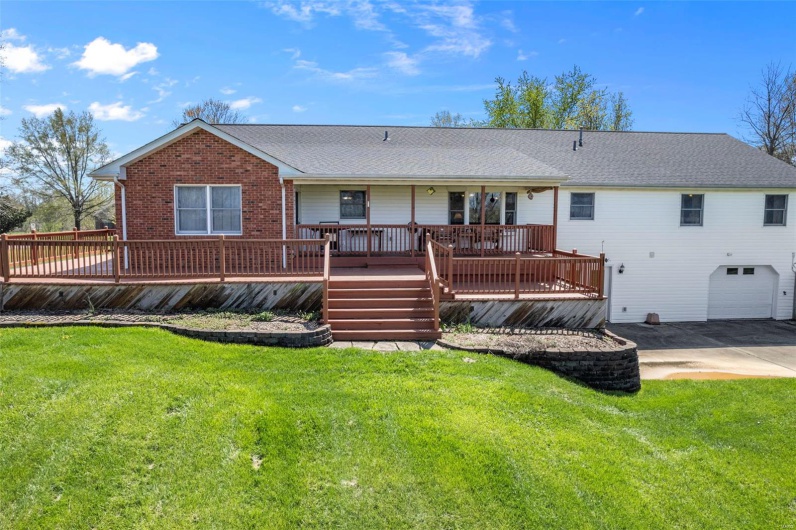 Rear view of house featuring an attached garage, a shingled roof, a deck, and a lawn
