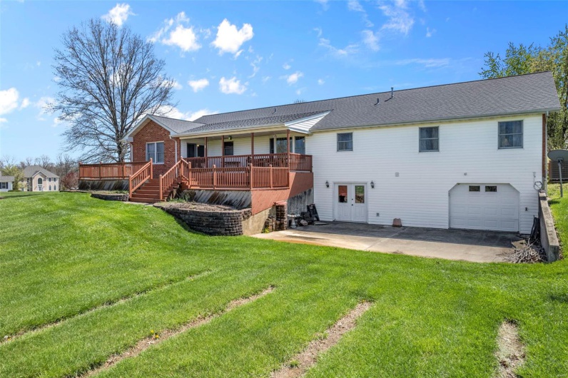 Back of property featuring driveway, a yard, a garage, and a deck