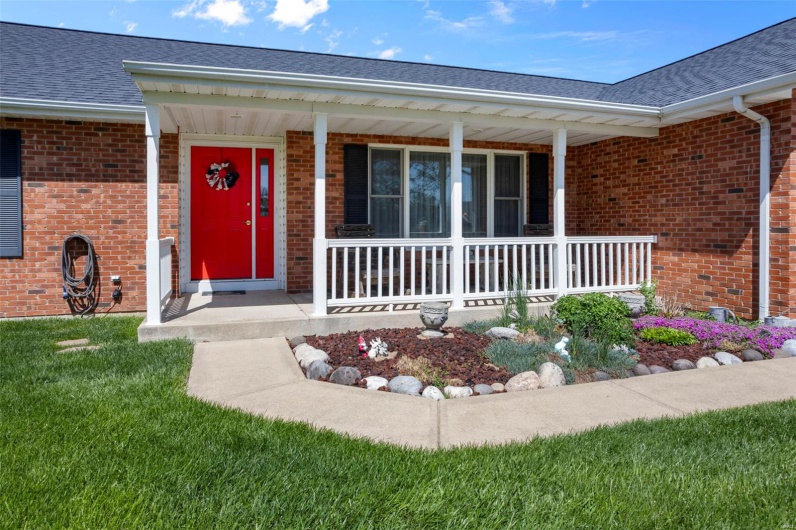 Property entrance featuring a porch, roof with shingles, a lawn, and brick siding