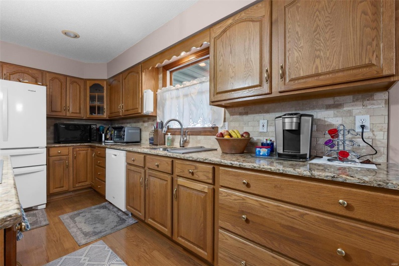 Kitchen featuring light stone counters, white appliances, brown cabinets, a sink, and wood finished floors