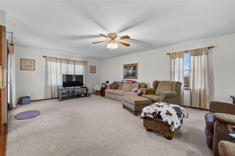 Carpeted living area featuring a textured ceiling, ceiling fan, and baseboards
