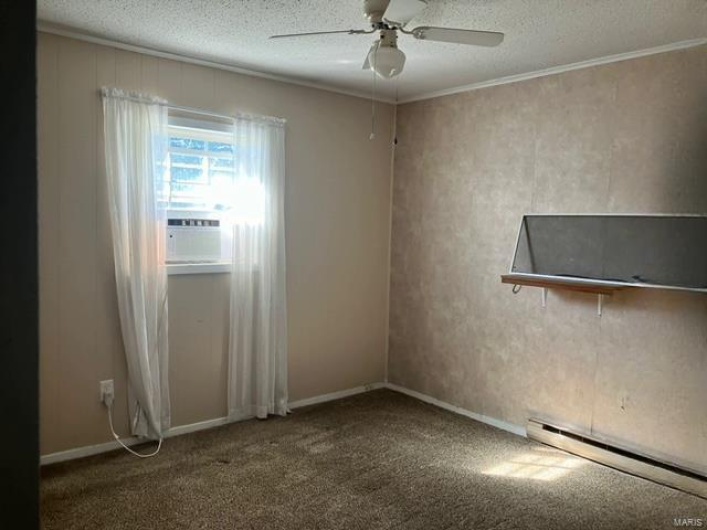 Carpeted empty room featuring a textured ceiling, cooling unit, a baseboard radiator, crown molding, and ceiling fan