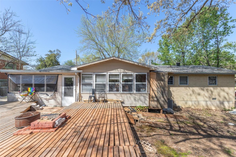 Back of property with brick siding, a wooden deck, a sunroom, and an outdoor fire pit