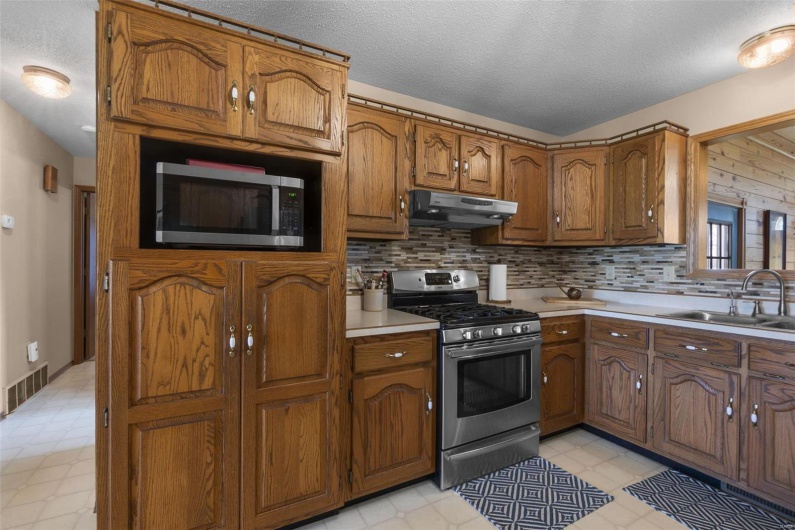 Kitchen featuring brown cabinets, under cabinet range hood, stainless steel appliances, visible vents, and a sink