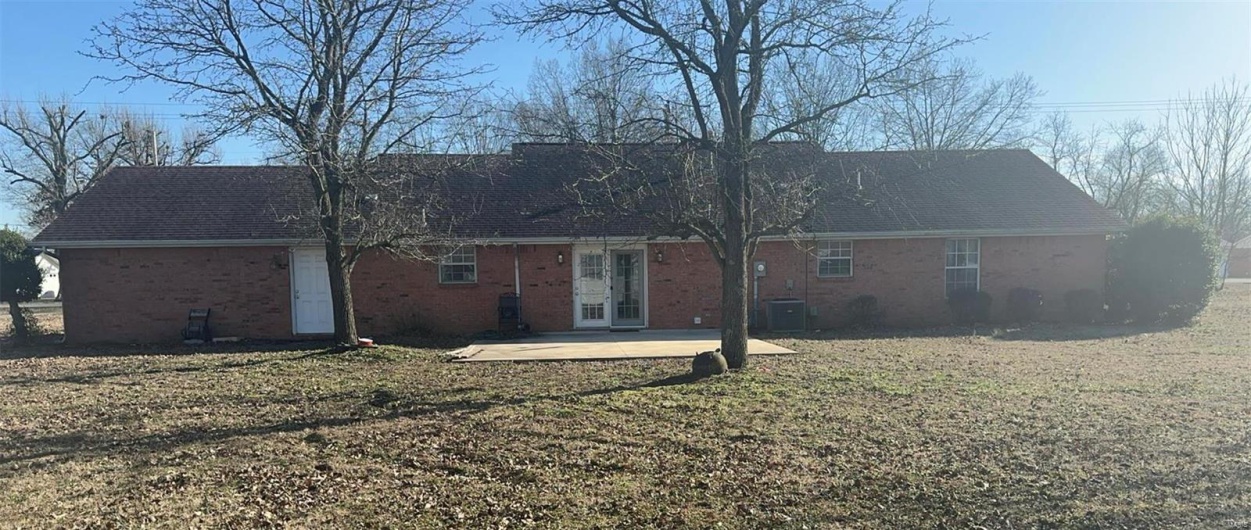 Rear view of house featuring central AC unit, brick siding, a shingled roof, a yard, and a patio area