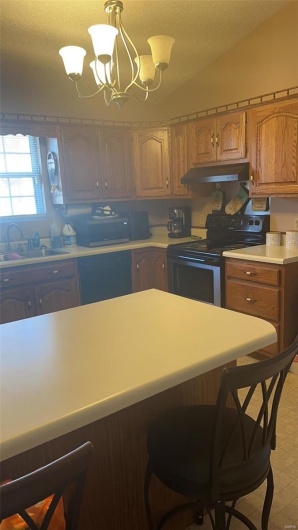 Kitchen with lofted ceiling, light countertops, a sink, stainless steel range with electric stovetop, and under cabinet range hood
