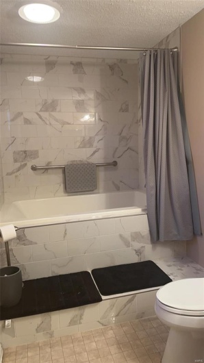 Bathroom with tiled shower / bath combo, a textured ceiling, and toilet