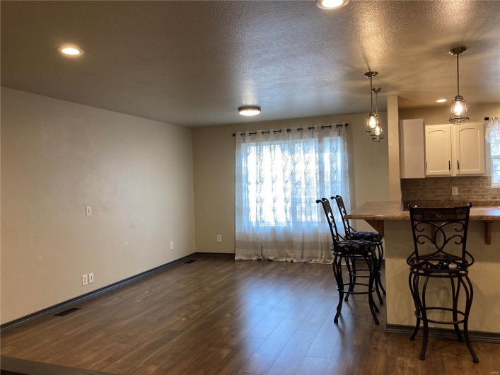 Kitchen featuring a breakfast bar area, dark wood finished floors, pendant lighting, white cabinetry, and backsplash
