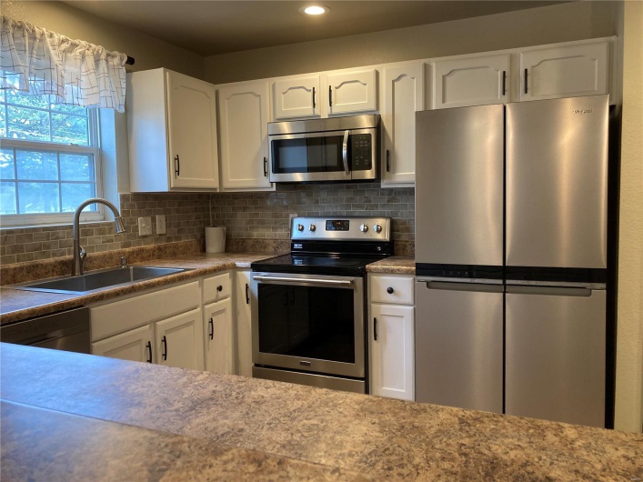 Kitchen with a sink, tasteful backsplash, appliances with stainless steel finishes, and white cabinets