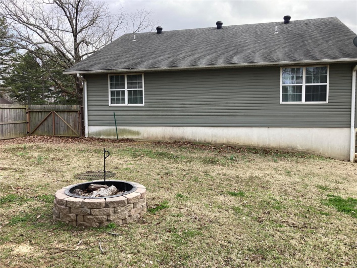 Back of house featuring a yard, an outdoor fire pit, a shingled roof, and fence