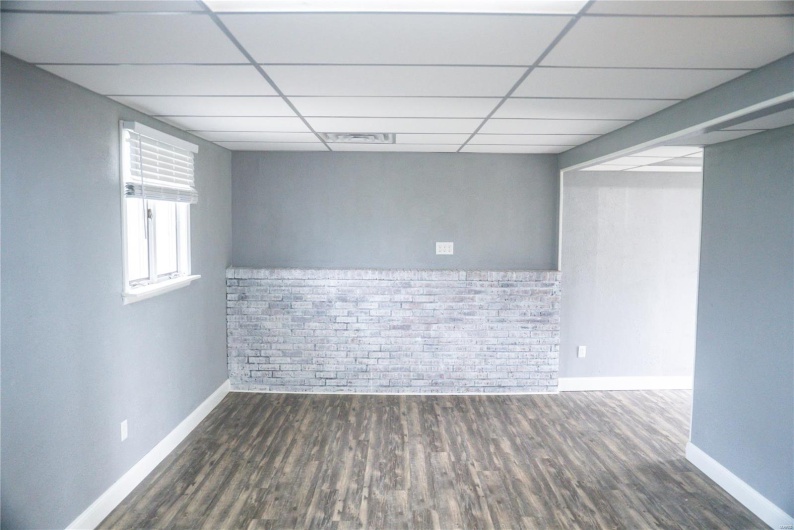 Empty room featuring baseboards, brick wall, visible vents, a drop ceiling, and wood finished floors