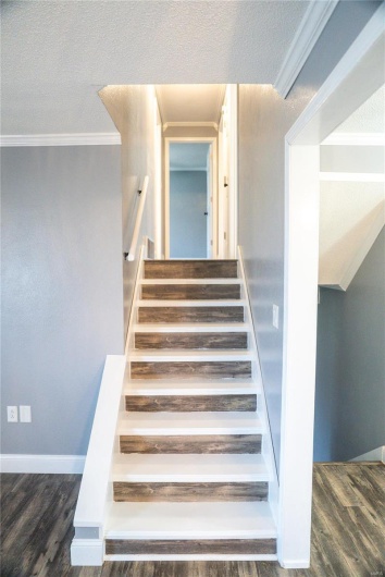 Staircase featuring ornamental molding, baseboards, wood finished floors, and a textured ceiling