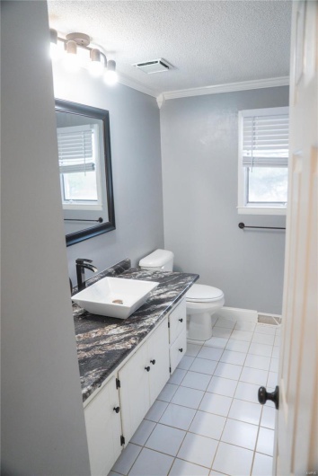 Half bathroom featuring vanity, ornamental molding, visible vents, toilet, and tile patterned floors