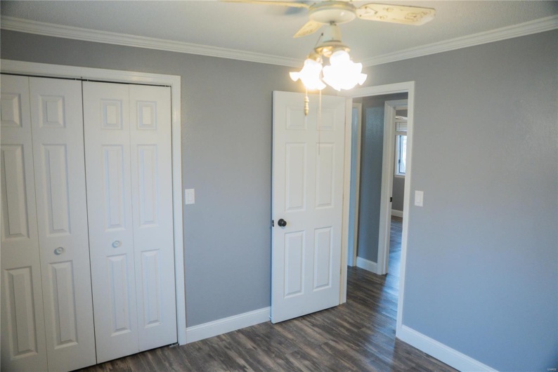 Unfurnished bedroom featuring a closet, baseboards, ornamental molding, dark wood-style floors, and ceiling fan