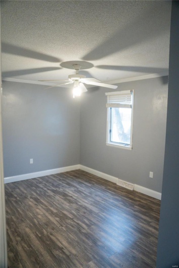 Empty room featuring dark wood-style flooring, baseboards, visible vents, and ceiling fan
