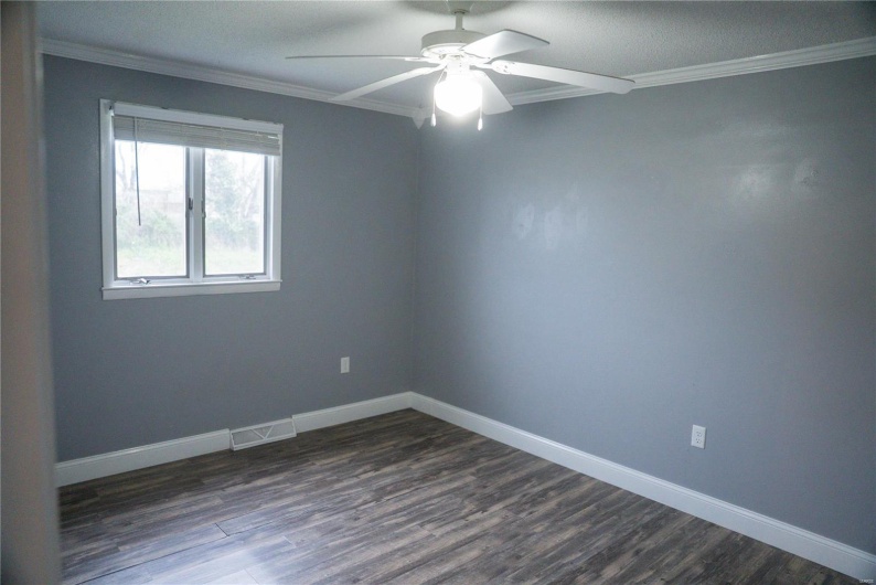 Unfurnished room featuring ornamental molding, a ceiling fan, visible vents, dark wood-style flooring, and baseboards