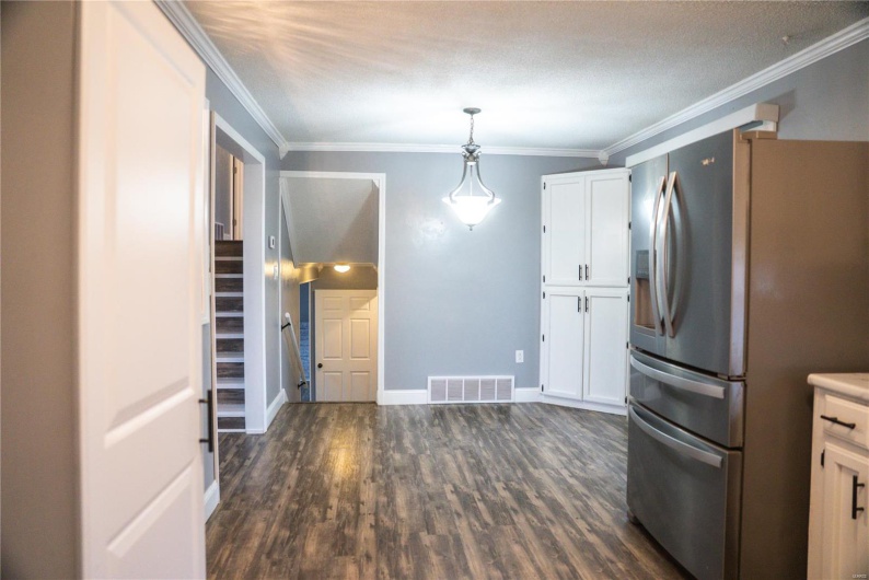 Kitchen featuring stainless steel fridge, dark wood-style floors, crown molding, white cabinets, and visible vents