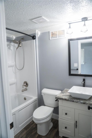Full bath with vanity, a textured ceiling, toilet, visible vents, and wood finished floors