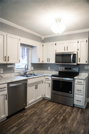 Kitchen with crown molding, appliances with stainless steel finishes, white cabinetry, and dark wood-type flooring