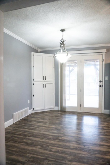 Empty room with dark wood-style flooring, visible vents, a textured ceiling, and crown molding