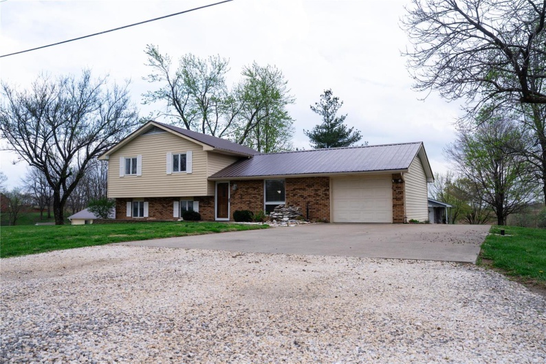 Tri-level home with a front yard, an attached garage, metal roof, brick siding, and driveway