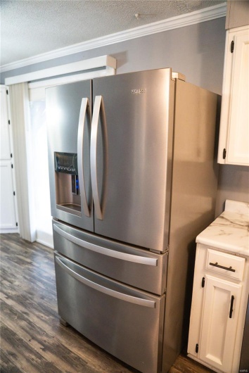 Details with stainless steel fridge with ice dispenser, a textured ceiling, ornamental molding, and white cabinetry