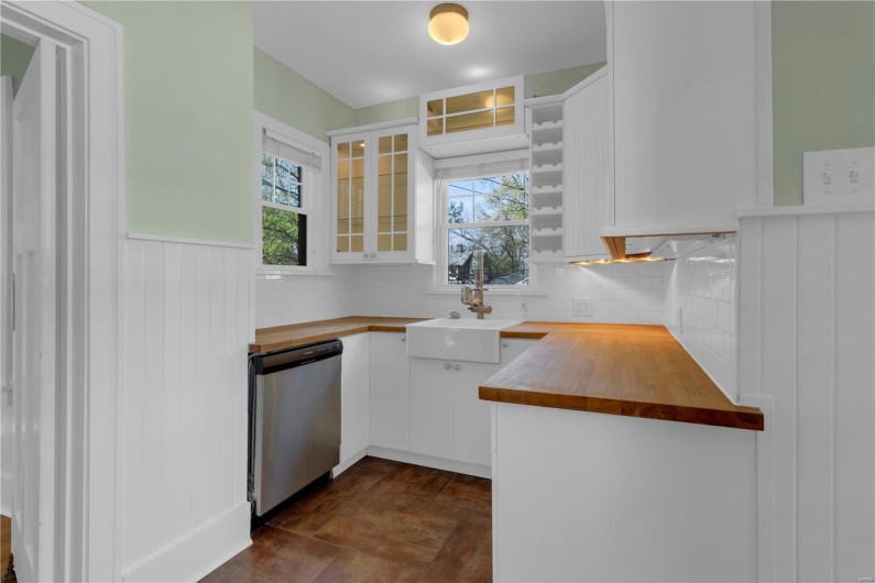 Kitchen featuring glass insert cabinets, stainless steel dishwasher, white cabinetry, and butcher block counters