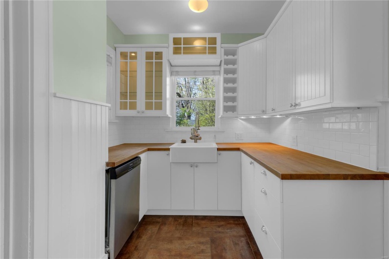 Kitchen with backsplash, butcher block counters, white cabinets, stainless steel dishwasher, and a sink