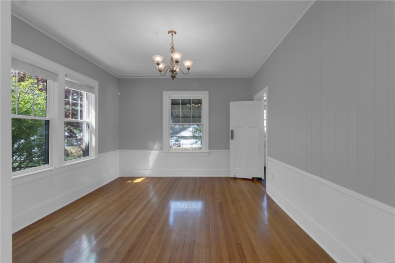 Spare room with a wealth of natural light, wood-type flooring, and an inviting chandelier