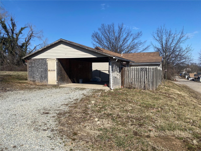 Garage featuring a carport, fence, and gravel driveway