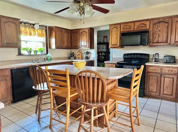 Kitchen with a kitchen breakfast bar, black appliances, light tile patterned flooring, light countertops, and a sink