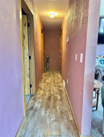 Hall featuring a textured ceiling, a textured wall, visible vents, and hardwood / wood-style flooring