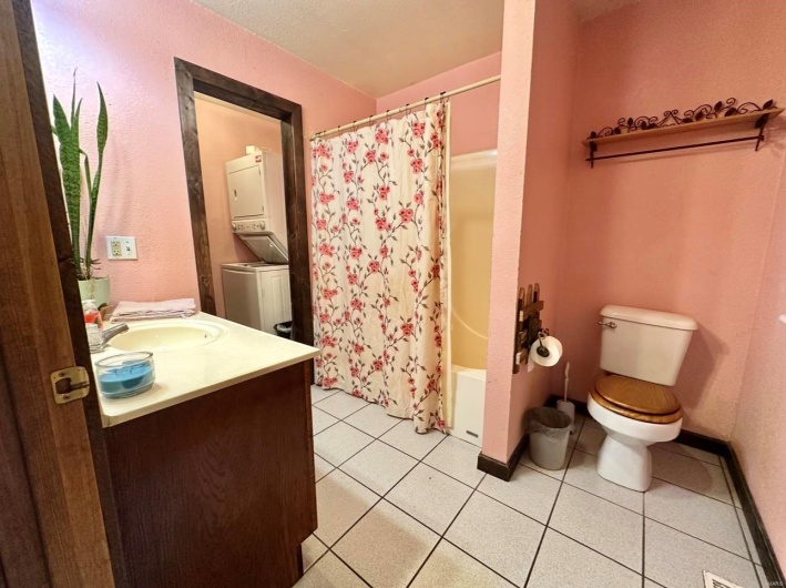 Bathroom featuring baseboards, toilet, stacked washer / drying machine, vanity, and tile patterned floors
