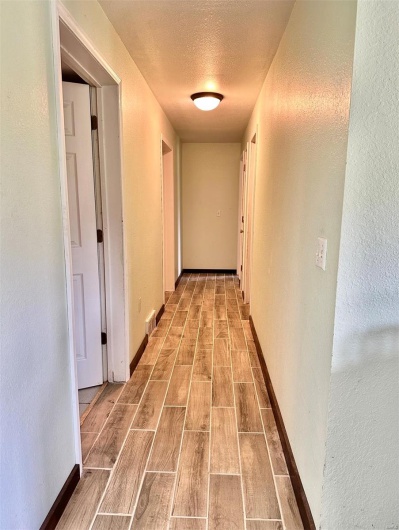 Hallway featuring wood finish floors, a textured ceiling, visible vents, a textured wall, and baseboards