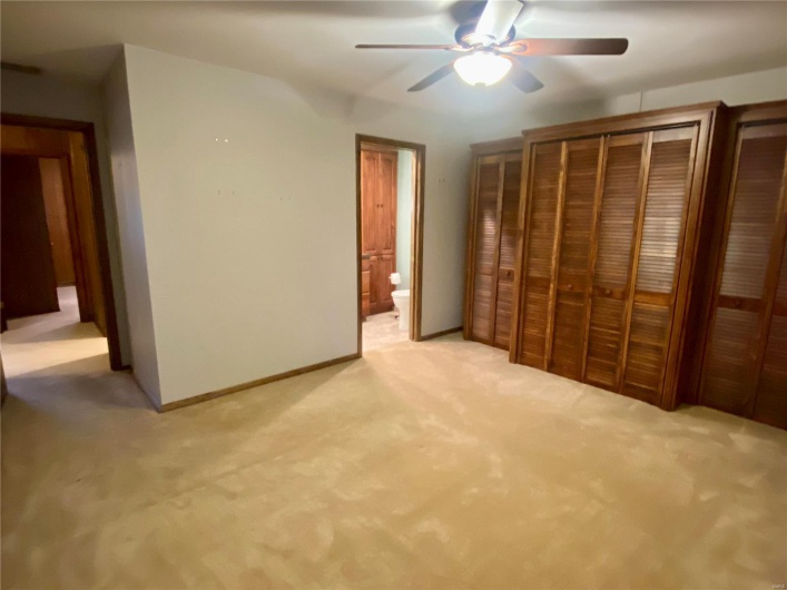 Unfurnished bedroom with light colored carpet, ensuite bath, and ceiling fan