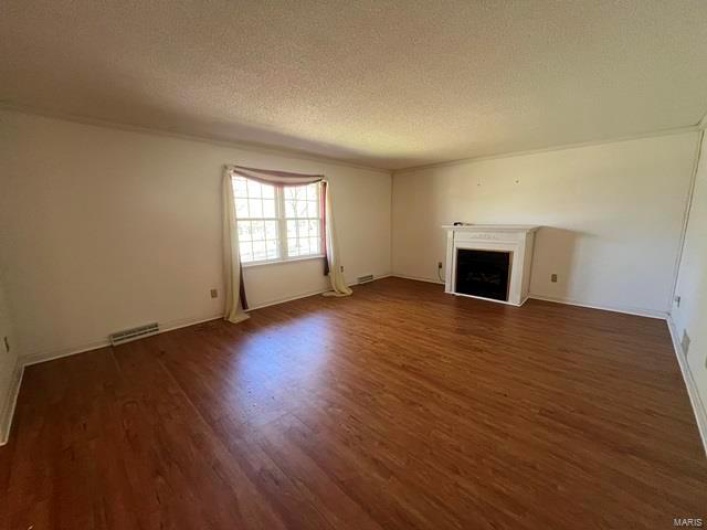Unfurnished living room with baseboards, a fireplace, a textured ceiling, visible vents, and wood finished floors