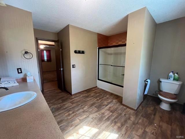 Full bathroom with a textured ceiling, shower / bath combination with glass door, vanity, toilet, and wood finished floors