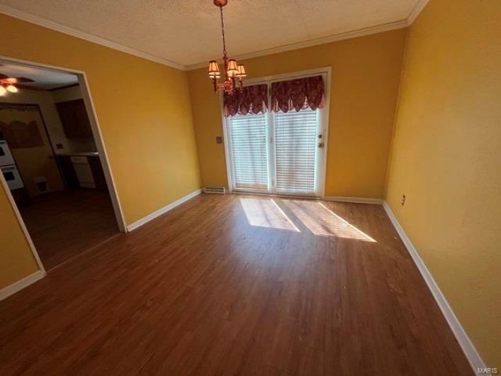 Unfurnished dining area with ornamental molding, baseboards, wood finished floors, and ceiling fan with notable chandelier