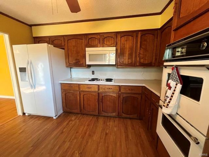 Kitchen with white appliances, light countertops, ornamental molding, and wood finished floors