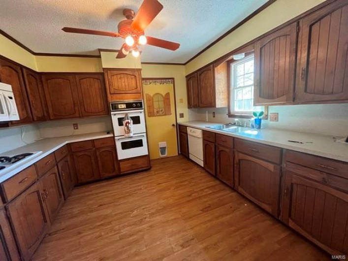 Kitchen featuring white appliances, light wood-style floors, a textured ceiling, and a ceiling fan