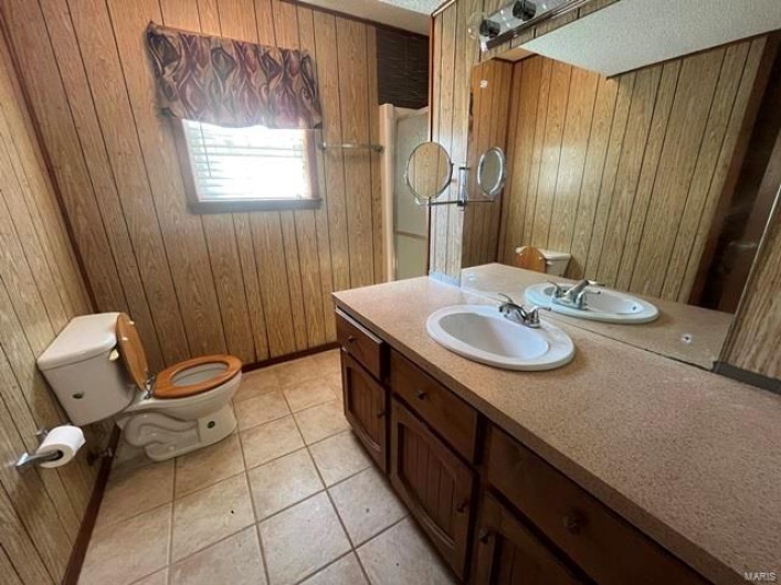 Bathroom with toilet, wooden walls, and tile patterned flooring