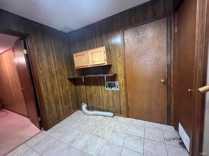 Laundry area with light tile patterned floors, wooden walls, washer hookup, and cabinet space