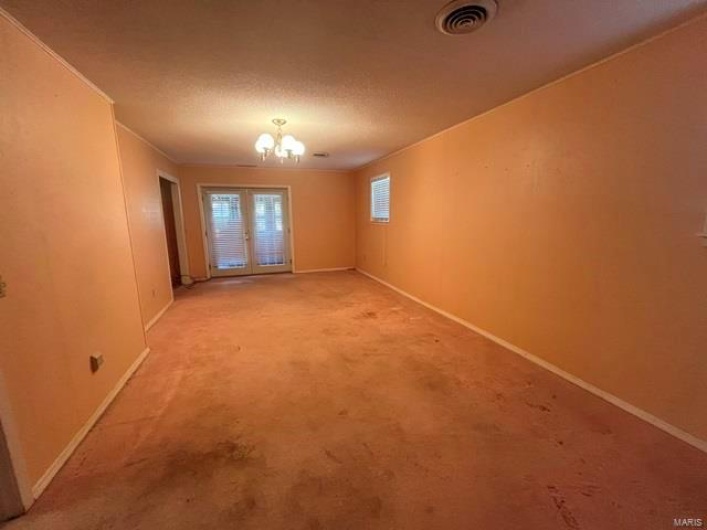 Empty room with light colored carpet, visible vents, a notable chandelier, and baseboards