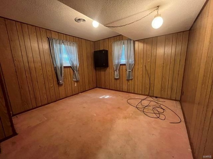 Unfurnished room with wooden walls, visible vents, and a textured ceiling